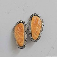 Pair of clip-on earrings with orange Spondylus shell and sterling silver bezel with decorative trim.