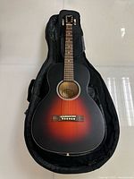 Front view of the sunburst finish Recording King 1930's style acoustic guitar inside a black padded soft gig bag.