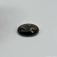 Front view of oval tiger's eye gemstone pin/brooch set in sterling silver with beaded edge detail.
