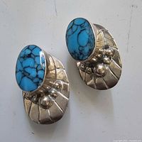 Pair of sterling silver clip-on earrings with bright blue simulated turquoise and bubble details on striated silver base, shown from angled top view.