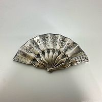 Front view of silver fan-shaped pin brooch showing engraved floral and leaf design.