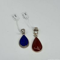 Two sterling silver pendants shown together, one with a lapis lazuli stone and one with a carnelian stone and pearl accent.