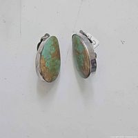 Pair of sterling silver clip-on earrings with drop-shaped turquoise stones, showing front view with green and yellow-brown marbled stones.