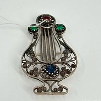 Front view of the vintage lyre-shaped pin showing the detailed filigree silverwork and red, green, and blue glass stones.