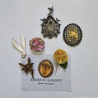 Photo showing seven vintage style brooches and pins arranged on white background with 'Eternal Garden Andrea Youngson' label.