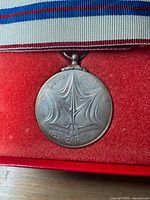 Reverse of medal showing stylized maple leaf design, ribbon and part of red case