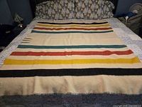 Full view of cream wool blanket laid on bed showing colored stripes and fringe edges