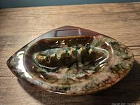 Top and angled views of a Beauceware ceramic ashtray with brown, green, and beige drip glaze on a wooden surface.