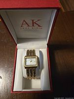 Anne Klein ladies goldtone wristwatch displayed in original red and white AK branded box on cushion.