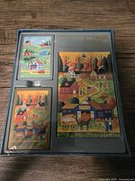 Top view photo showing two decks of playing cards and the matching cardstock in a plastic tray with folk art rural scene design featuring houses, trees, horses, and pumpkin patches under a sun.