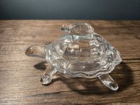 Clear glass trinket dish shaped as a turtle with a smaller baby turtle figure on its back shown from a side angle.