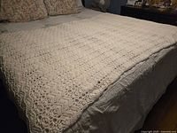 Full view of crocheted cream throw spread on bed showing intricate stitch work and detail.