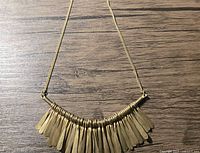 Close-up photo of the brass necklace showing multiple elongated pendants hanging from a curved bar on a wooden surface.