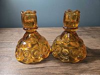 Pair of amberina glass L.E. Smith Moon and Stars candlestick holders on wood surface, front angle