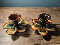 Two vintage multicolored ceramic drip glaze flower-shaped candlesticks with scalloped candle holders shown side by side on wooden surface