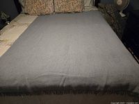 Full view of the grayish blue wool throw blanket spread on a bed showing overall condition and color.