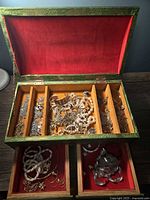 Open view of jewelry box showing multiple compartments filled with mixed costume jewelry including necklaces, bracelets, and earrings.
