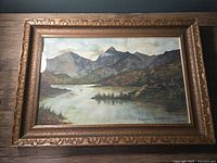 Full view of the landscape painting in ornate carved wooden frame showing mountain and lake scenery.