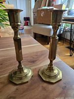 Pair of vintage solid brass candlesticks shown upright on a wooden surface, visible octagonal bases and columnar stems with original patina.