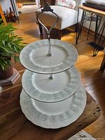 Three tiered dessert stand made of fine bone china in the Paragon Melanie pattern, shown in natural lighting on wooden floor near furniture and plants.