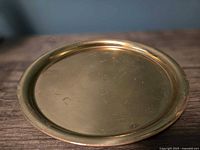 Top view of a round brass serving tray showing some surface wear and scratches, placed on a wooden surface.