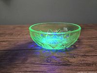 Small green glowing Hazel Atlas uranium glass bowl with star-shaped cut depression pattern glowing under UV light on wooden surface.