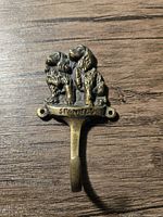 Front view of brass hook showing two spaniel dogs sitting side by side with the word 'SPANIELS' beneath them, mounted on a wooden surface.