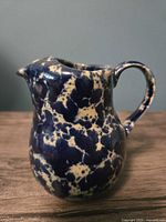 Front left view of the speckled mini pitcher showing the spout and handle, highlighting the blue and cream speckled pattern.
