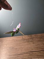 Side view of the hummingbird showing vibrant painted wings and translucent hanging string.