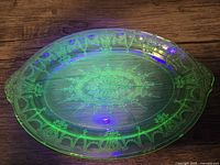Top view of oval green uranium glass platter showing intricate ballerina cameo pattern and central medallion design glowing under UV light.