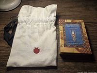 White cloth drawstring bag with a red circular emblem on a wooden surface.