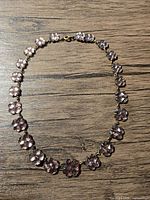 Full view of vintage brass necklace showing purple gem stones shaped like four-leaf clovers laid flat on wood surface