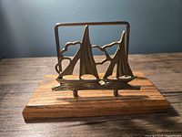 Front view of the vintage brass and wood holder with a brass sailboat design on a wooden base.