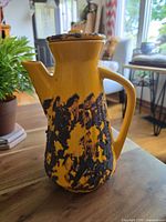 Front view showing bulbous body with thick orange glaze and black textured lava pattern, handle, and spout.