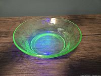 Top view of translucent green uranium glass fruit bowl glowing under UV light, showing floral embossed details.
