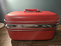 Exterior front view of red makeup case with chrome locking mechanism and no keys.