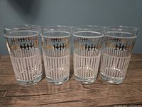 Front view of four vintage Dominion glasses with white and gold patterns on wooden surface.
