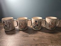 Four ceramic mugs arranged showing two of each floral design, cream colored with colorful flowers and brown trim.
