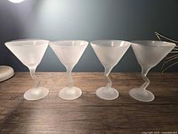 Front view of all four vintage frosted martini glasses with zigzag stems lined up against a grey-blue wall.