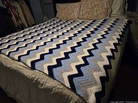 Full bed covered with vintage handmade crocheted wool throw blanket showing overall pattern and colors.