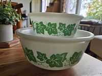 Side view showing two nesting milk glass mixing bowls with green ivy leaf pattern