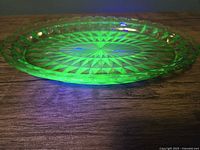 Side view showing shallow oval shape and scalloped edge of uranium glass tray glowing under black light