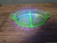 Photo of oval green uranium glass divided relish dish glowing under UV light showing floral pattern and handles