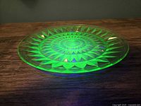 Side view of vintage uranium glass Windsor Diamond tray showing raised edge and geometric pattern glowing bright green under UV light.