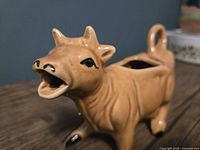 Front angled view of the brown ceramic cow-shaped coffee creamer showing the open mouth pouring spout and facial features.