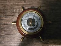 Top view of vintage ship's wheel barometer showing dial with weather indicators.