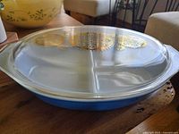 Side view of blue divided Pyrex casserole dish with clear lid showing gold pattern and dish handles