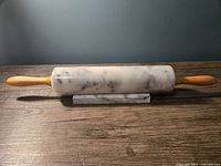 Marble rolling pin with wooden handles resting on the matching marble stand on a wooden surface under soft lighting.