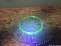 Top view of octagonal uranium glass tray glowing green under UV light, showing two handles and visible surface scratches.