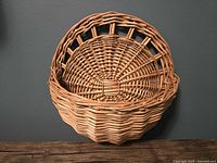 Front view of larger vintage wicker wall basket against wall and wood surface